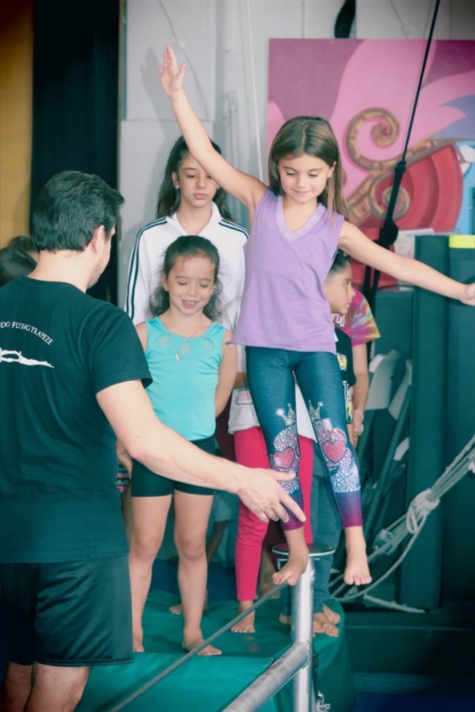 Coach guiding a child on a balance beam at circus camp