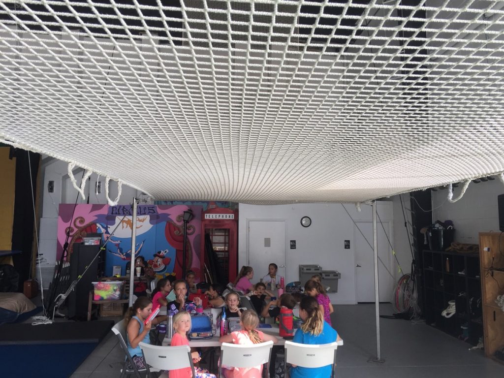 Campers taking a break at tables under the safety net at circus camp